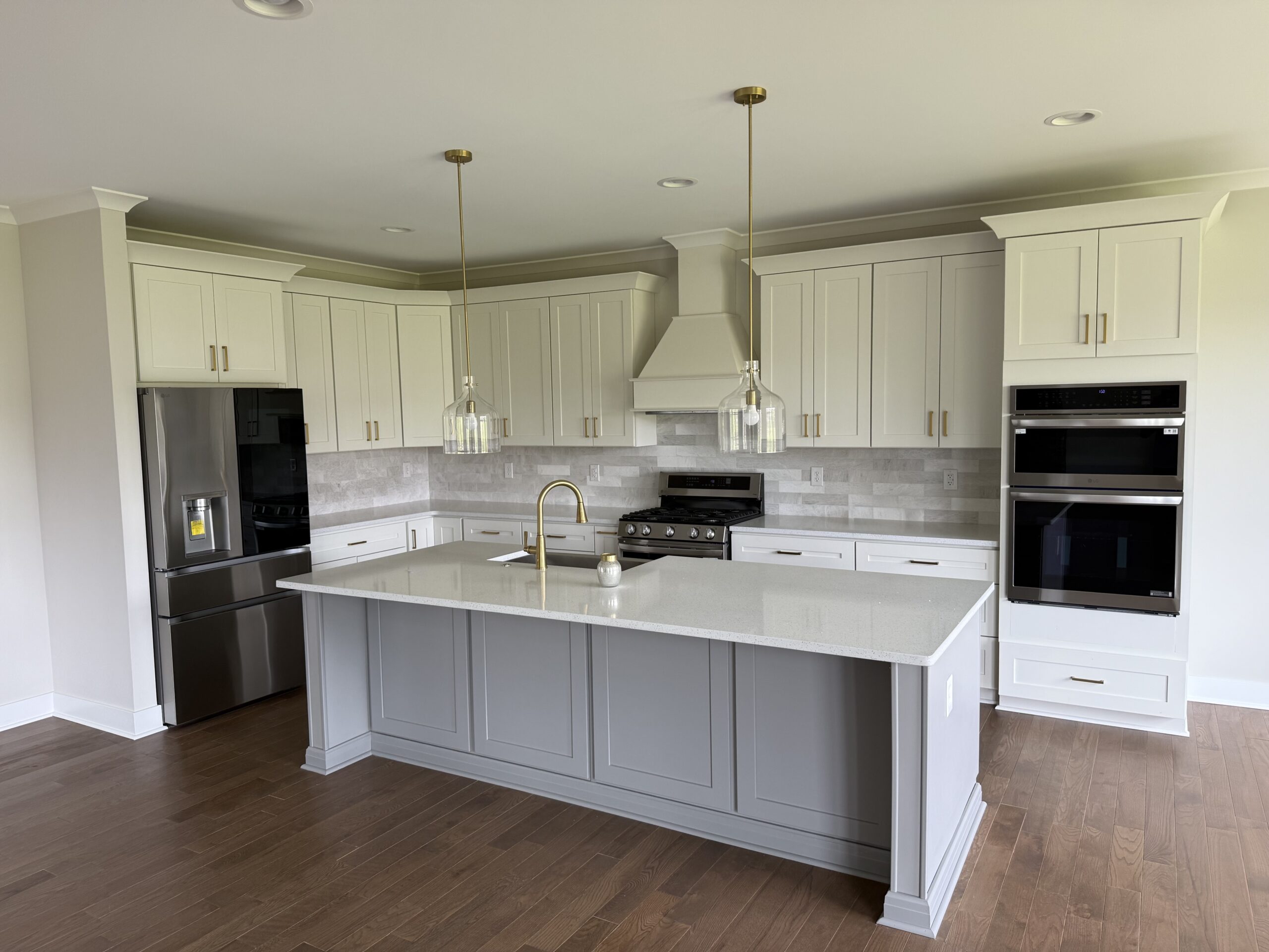 Bright white kitchen remodel with large island, white cabinets, tile backsplash, built-in appliances, lighting, and finished flooring by Alabaster Contracting Solutions